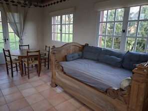 Ein Zimmer mit einem hölzernen Bett, einem Esstisch mit Stühlen und großen Fenstern.