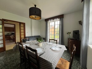 A dining area with a table set for four, chairs, a hanging light fixture, and a view through a window.