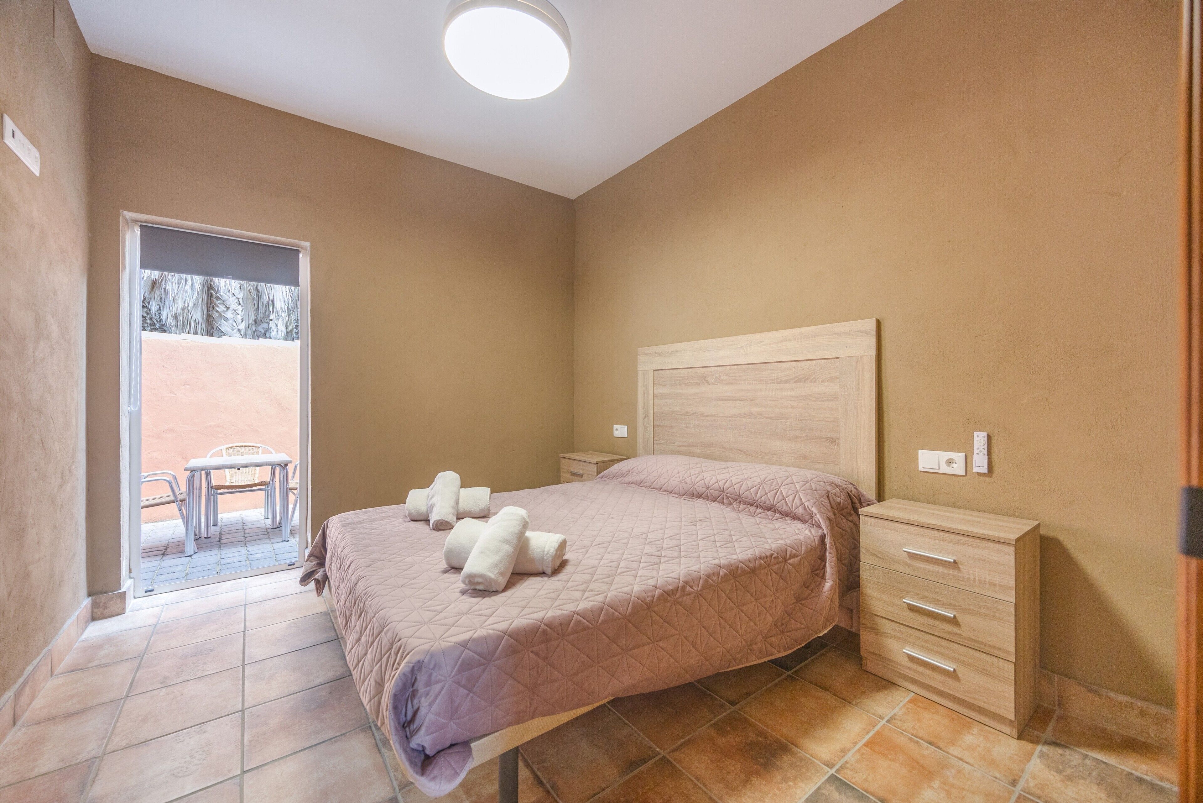 Une chambre à coucher avec un lit, une table de chevet, une chaise et une vue sur l’extérieur.