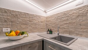 A modern kitchen with a stone backsplash, a sink, and a bowl of fruit on the counter. - Seaside Apartment 'Trifamiliare Garden - Conchiglia' with Private Terrace, Wi-Fi & AC (Agnone)