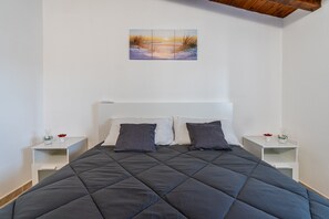 Une chambre à coucher avec un lit, deux tables de chevet, une commode, un tableau et une poutre en bois au plafond.