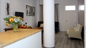 Ein modernes Wohnzimmer mit einem Holztisch, einem beigefarbenen Sessel, einem Fernseher und einem großen Fenster.