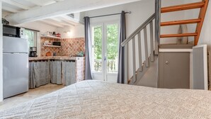 Une chambre avec une couvre-lit à motifs, une cuisine équipée d’un réfrigérateur, d’une cuisinière et d’étagères, et un escalier menant à un étage supérieur.