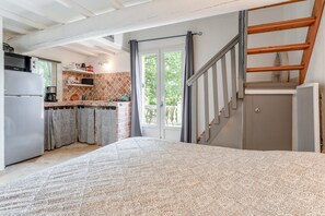 Un dormitorio con una colcha estampada, una cocina con refrigerador, estufa y estantes, y una escalera que conduce a un nivel superior.