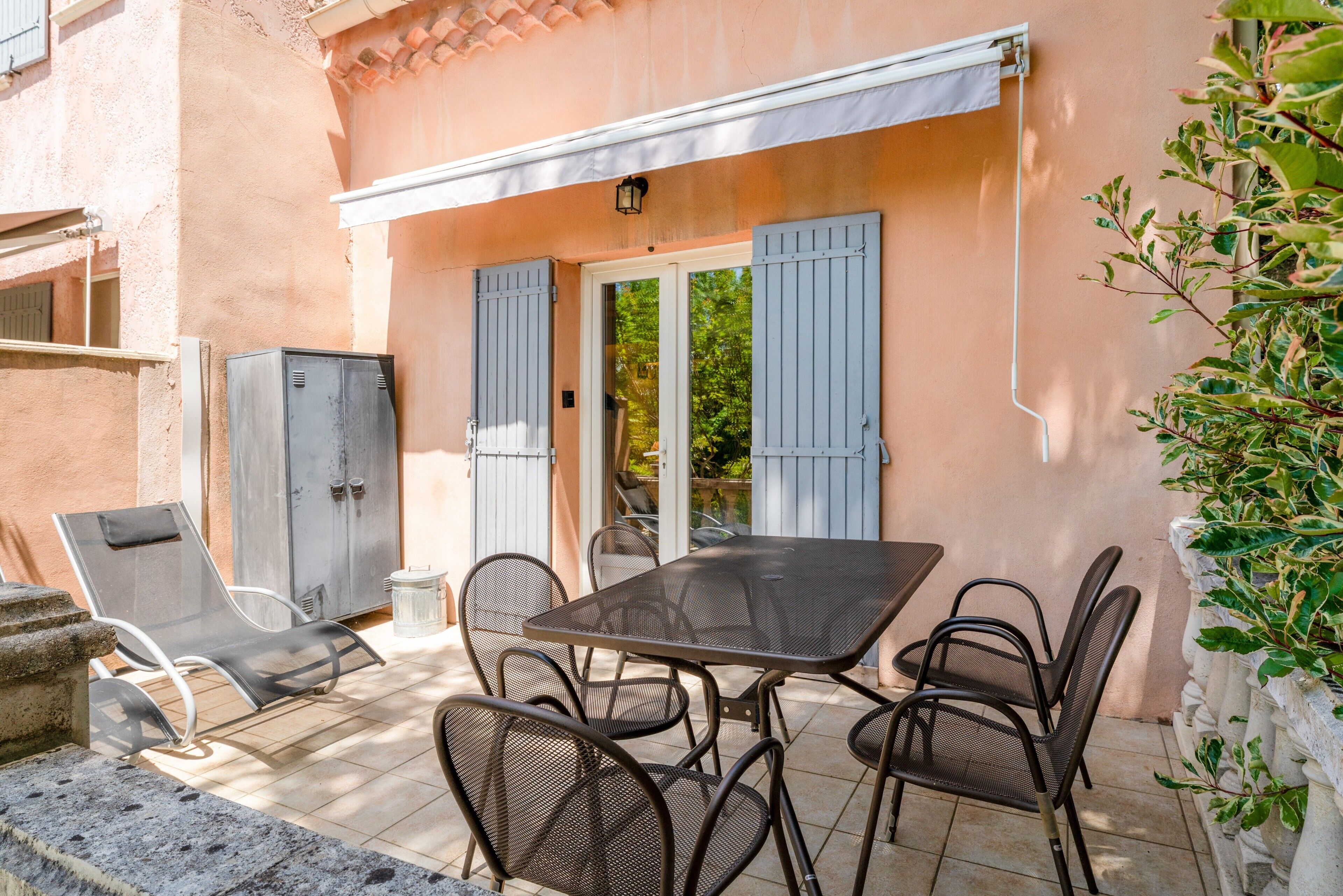 Une terrasse extérieure avec une table et des chaises, une porte et un mur avec des volets.