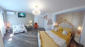 Un dormitorio con una cama grande, una silla, una mesita pequeña, un televisor montado en la pared y una puerta.