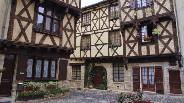 Un edificio tradicional con entramado de madera, entrada de piedra, contraventanas de madera y macetas con flores.