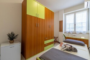 A bedroom with a bed, a wardrobe, a radiator, a window with curtains, and a small plant.
