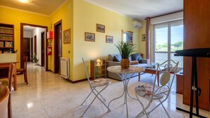 Una sala de estar con un sofá, una mesa de comedor con sillas, una mesita redonda con una planta y una zona de cocina con armarios.