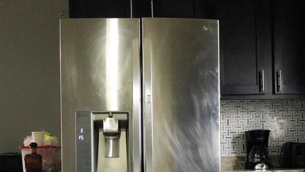 Un refrigerador de acero inoxidable con dispensador de agua, una cafetera y un piso de cocina con baldosas.