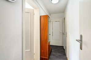 A narrow hallway with white walls, a wooden wardrobe, and a white door at the end.