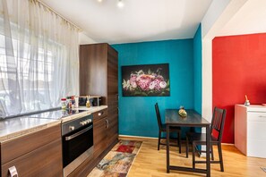 A modern kitchen with wooden cabinets, a dining table with chairs, and a painting on the wall.