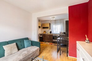 A compact living space with a kitchenette, a green sofa, and a red accent wall.