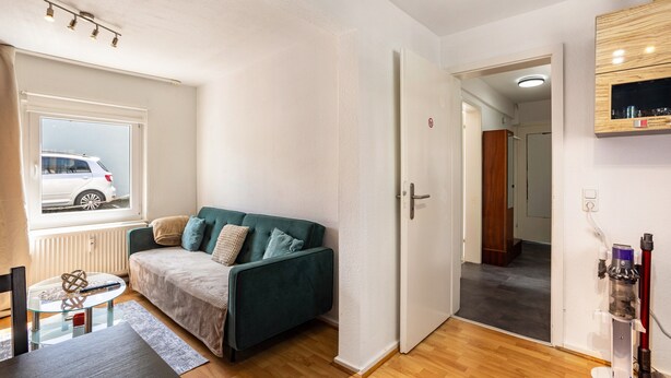 A modern living room with a green sofa, a glass coffee table, and a view of a white car outside. - Apartment “Central Hemer Near Lung Clinic” with Wi-Fi (Hemer)