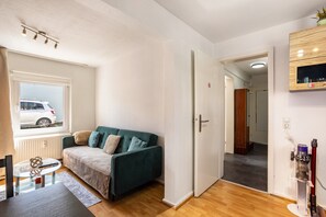 Ett modernt vardagsrum med en grön soffa, ett soffbord i glas och utsikt över en vit bil som står parkerad utanför.