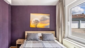 A bedroom with a bed, a nightstand, a window with curtains, and a wall painting. - Apartment “Central Hemer Near Lung Clinic” with Wi-Fi (Hemer)