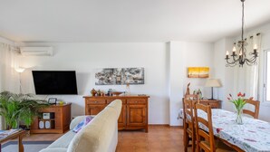 A living room with a sofa, TV, wooden cabinet, dining table with chairs, and a chandelier. - Semi-detached house with sea views and communal pool (Begur)