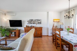 A living room with a sofa, TV, wooden cabinet, dining table with chairs, and a chandelier. - Semi-detached house with sea views and communal pool (Begur)