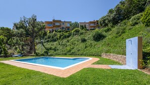 A swimming pool with a stone border, surrounded by grass, with a building in the background. - Semi-detached house with sea views and communal pool (Begur)