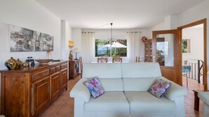 A living room with a sofa, wooden cabinets, a dining area, and a view of the outdoors. - Semi-detached house with sea views and communal pool (Begur)