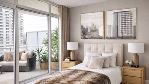 A bedroom with a large bed, two bedside tables, a sofa, and a view of a cityscape through a sliding glass door. - Ocean View Downtown (White Rock)