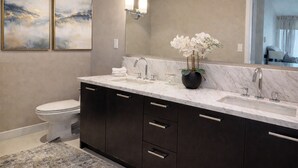 A bathroom with a marble sink, dark cabinets, a toilet, and two framed artworks on the wall. - Ocean View Downtown (White Rock)