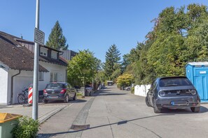 Une rue résidentielle bordée de voitures garées, avec des toilettes publiques portables bleues et un vélo.
