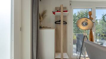 Une pièce dotée d’une porte-fenêtre coulissante donnant sur un espace extérieur, d’un luminaire suspendu et d’une étagère en bois ornée d’objets décoratifs.