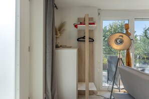 Une pièce dotée d’une porte-fenêtre coulissante donnant sur un espace extérieur, d’un luminaire suspendu et d’une étagère en bois ornée d’objets décoratifs.