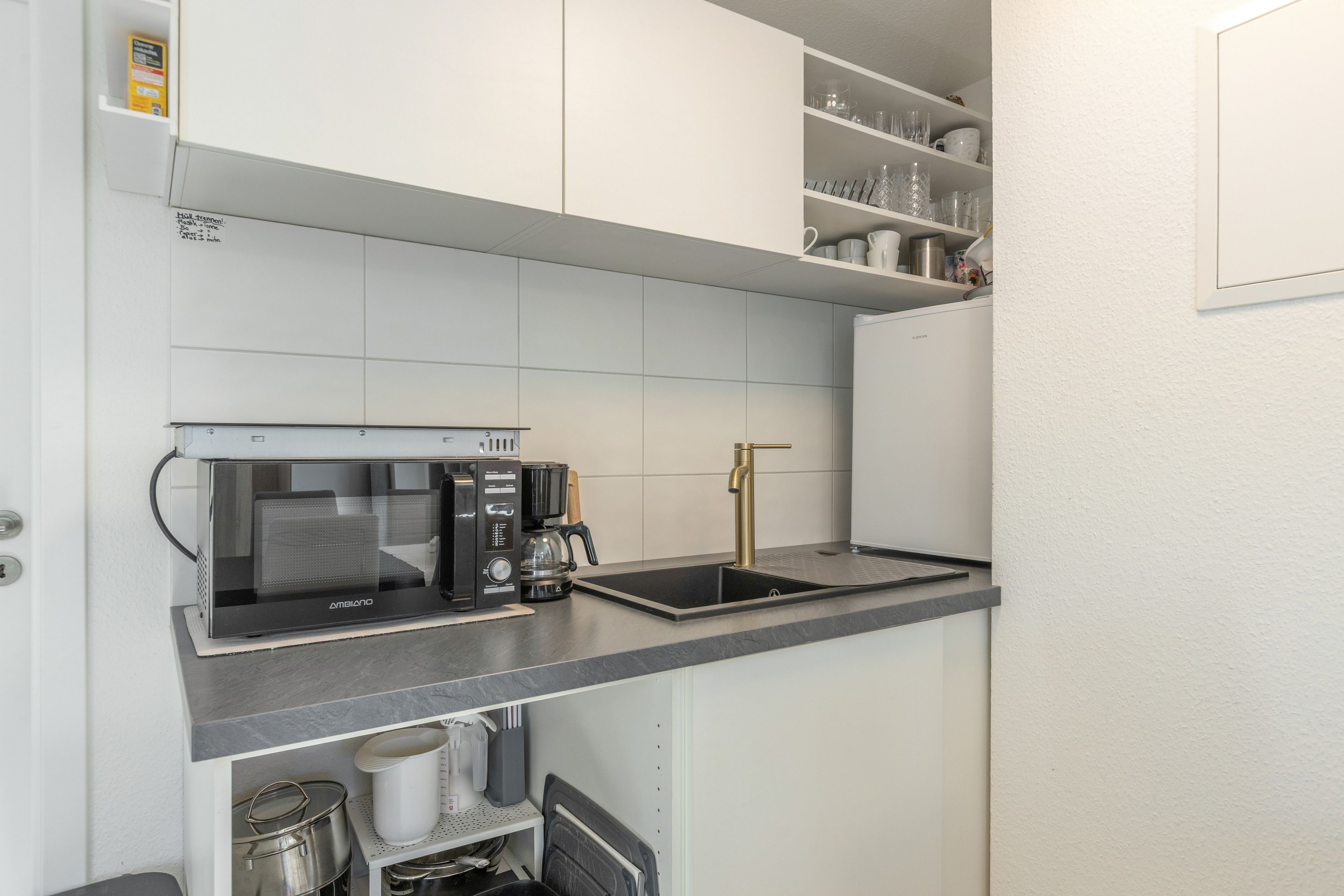 A compact kitchen with a built-in microwave, coffee maker, and a stainless steel sink.