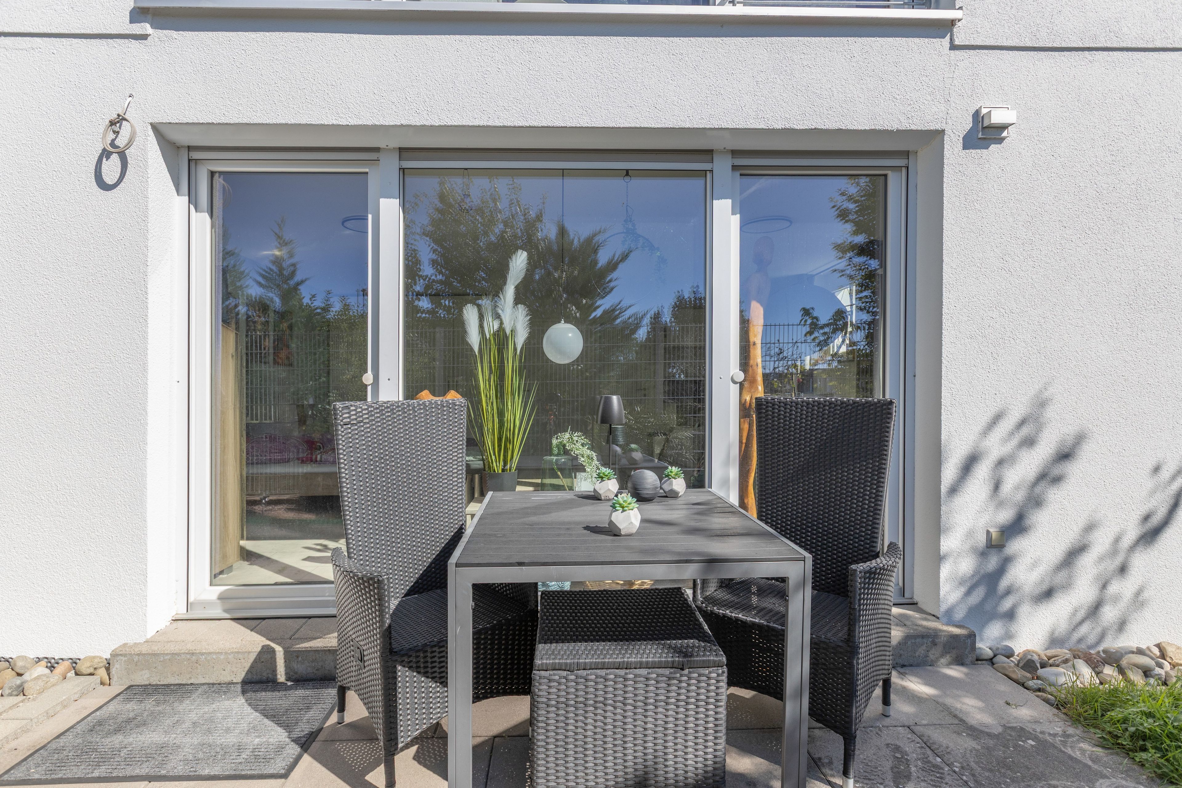 Une terrasse avec une table et des chaises, une plante en pot et une vue à travers une porte vitrée.