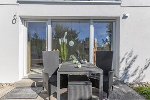 Une terrasse avec une table et des chaises, une plante en pot et une vue à travers une porte vitrée.