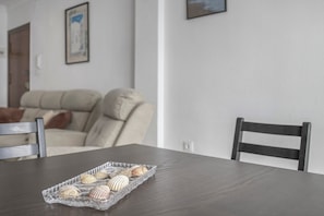 Uma mesa de jantar com uma bandeja de conchas, uma cadeira de madeira e um sofá ao fundo.