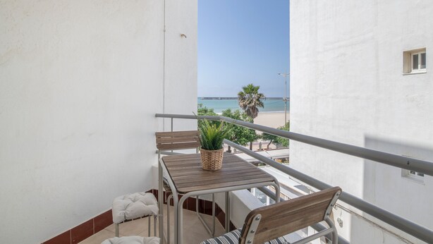 A balcony with a table, chairs, a potted plant, and a view of the beach. - Apartment 'Marítimo' with Sea Views and Private Terrace (Barbate)