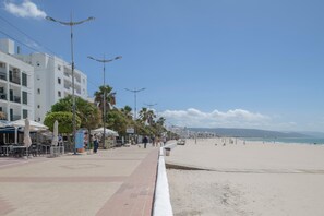 A beachside promenade with outdoor seating, palm trees, and a clear sky.