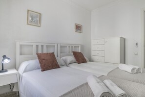 A bedroom with a white bed, two pillows, a nightstand with a lamp, a dresser, and two framed pictures on the wall.