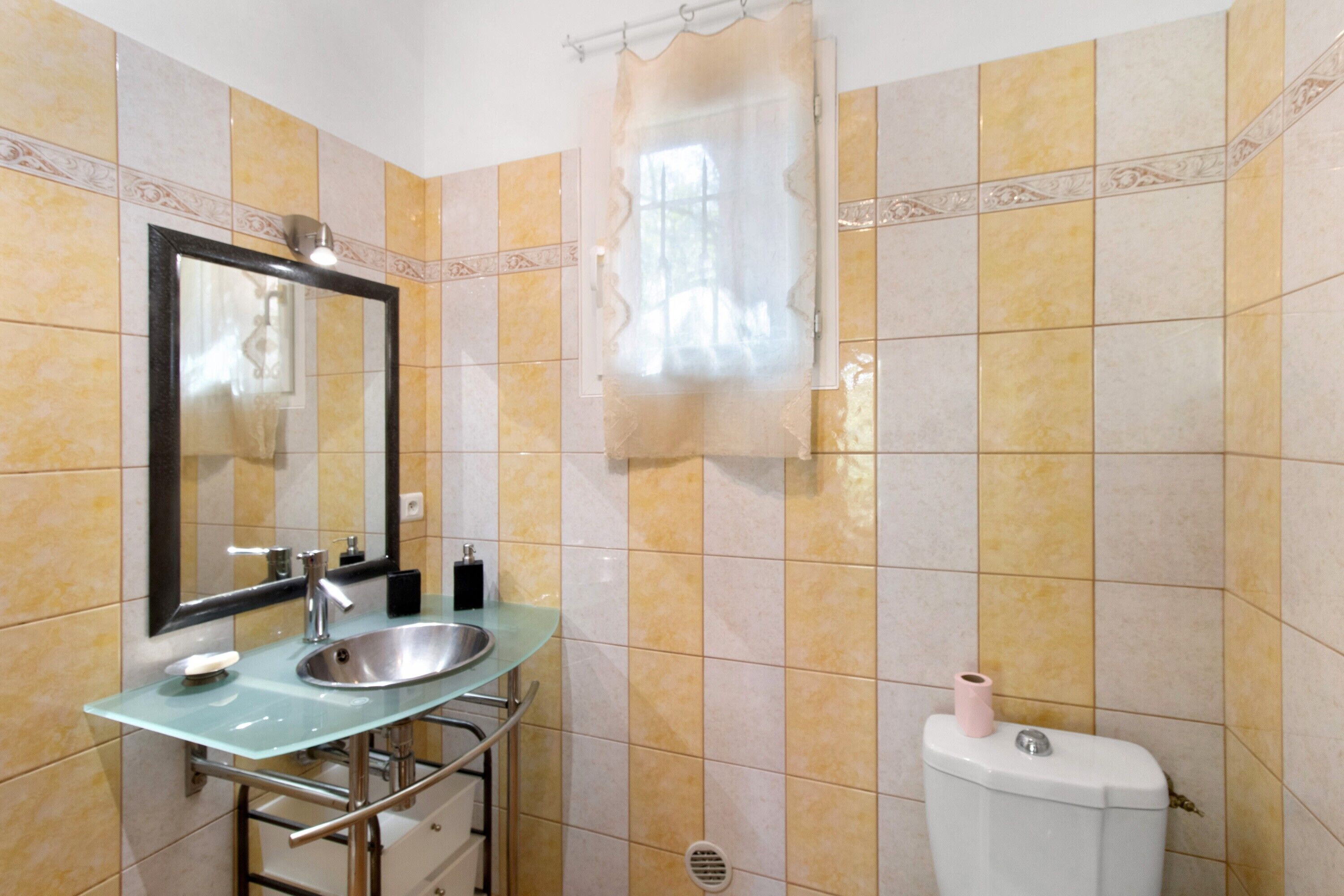 A bathroom with a glass sink, a mirror, a toilet, and a shower curtain.