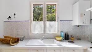 Une cuisine équipée d’un évier à deux bacs, d’un lave-linge et d’une fenêtre agrémentée de rideaux en dentelle.