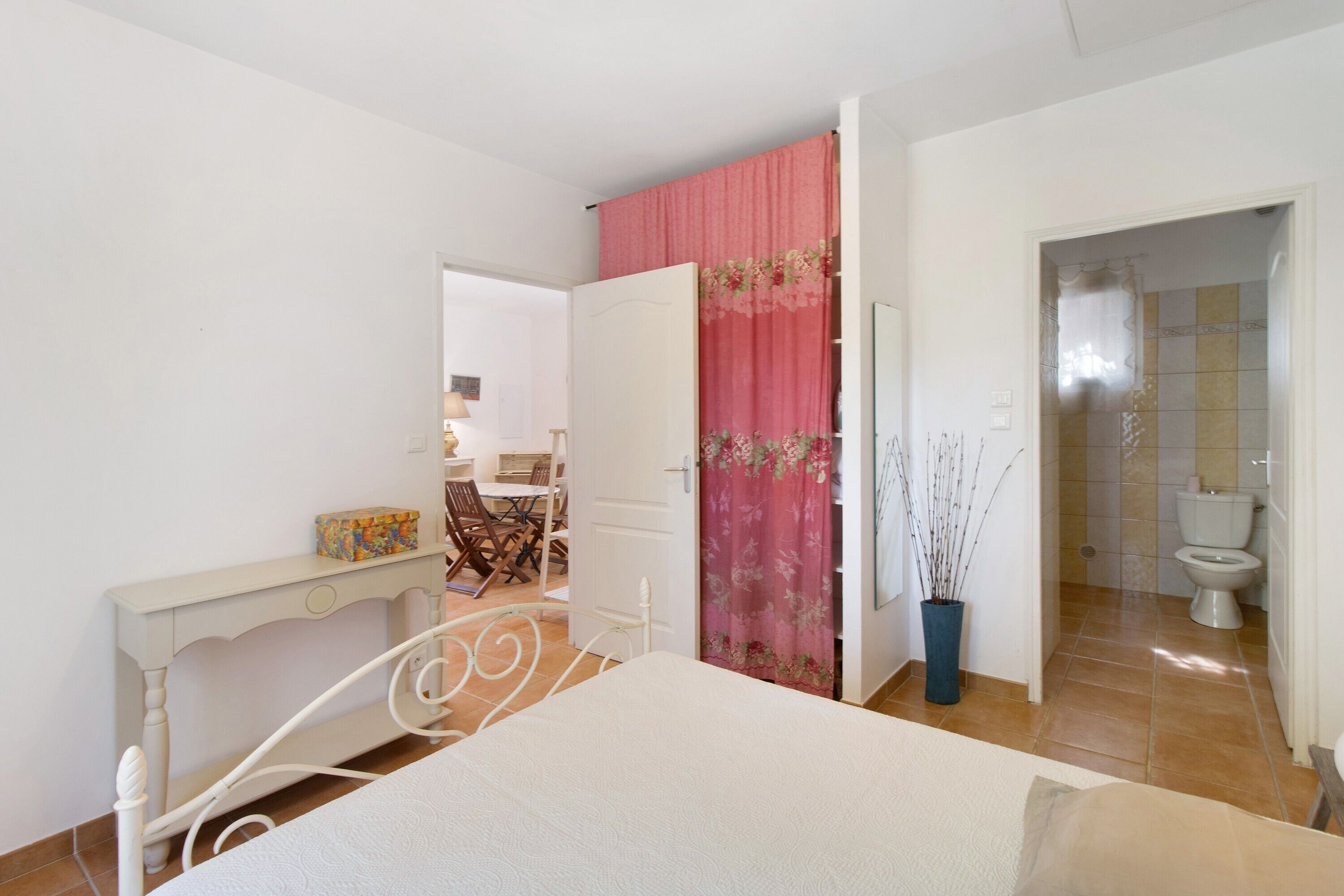 Un dormitorio con cama, escritorio, silla, armario y baño con inodoro y ducha.