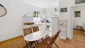 Une cuisine avec des meubles blancs, une table à manger, des chaises et une horloge au mur.