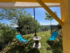 Zona relax all'aperto con due sedie blu, un tavolo e vista su un paesaggio verde.