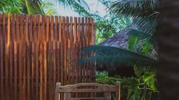 A wooden bench in a shaded outdoor area with a wooden fence and tropical plants.