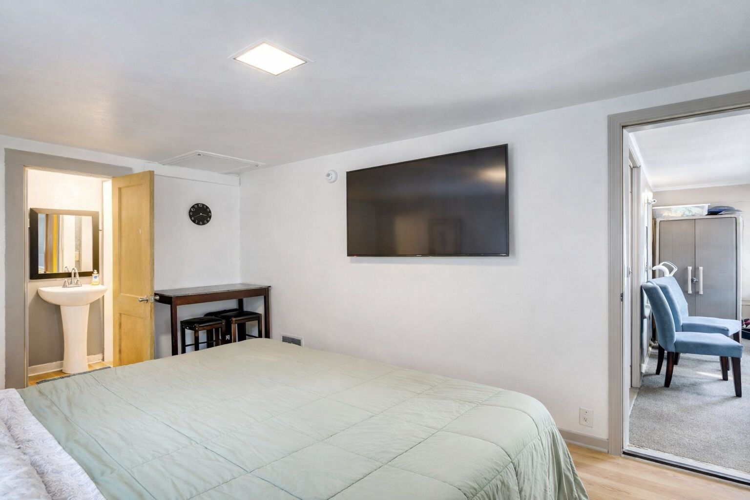 A bedroom with a bed, a desk, a TV, a wardrobe, and a bathroom with a sink and mirror.