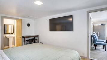 A bedroom with a bed, a desk, a TV, a wardrobe, and a bathroom with a sink and mirror.