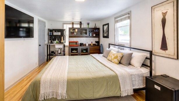 Un dormitorio con cama, televisor, kitchenette y un cuadro en la pared.