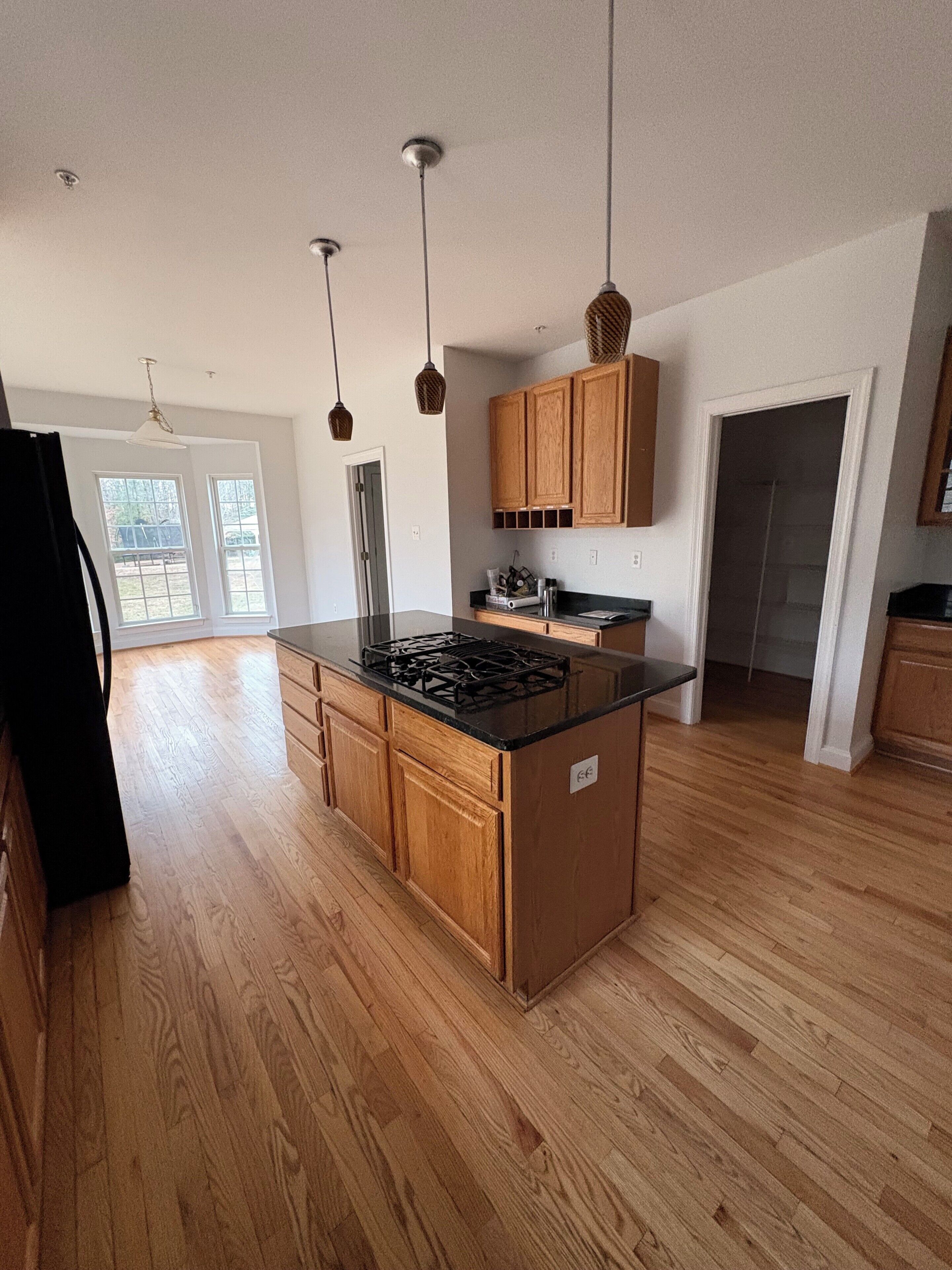 A modern kitchen with wooden cabinets, a central island with a stove, pendant lighting, and a view to the outside.