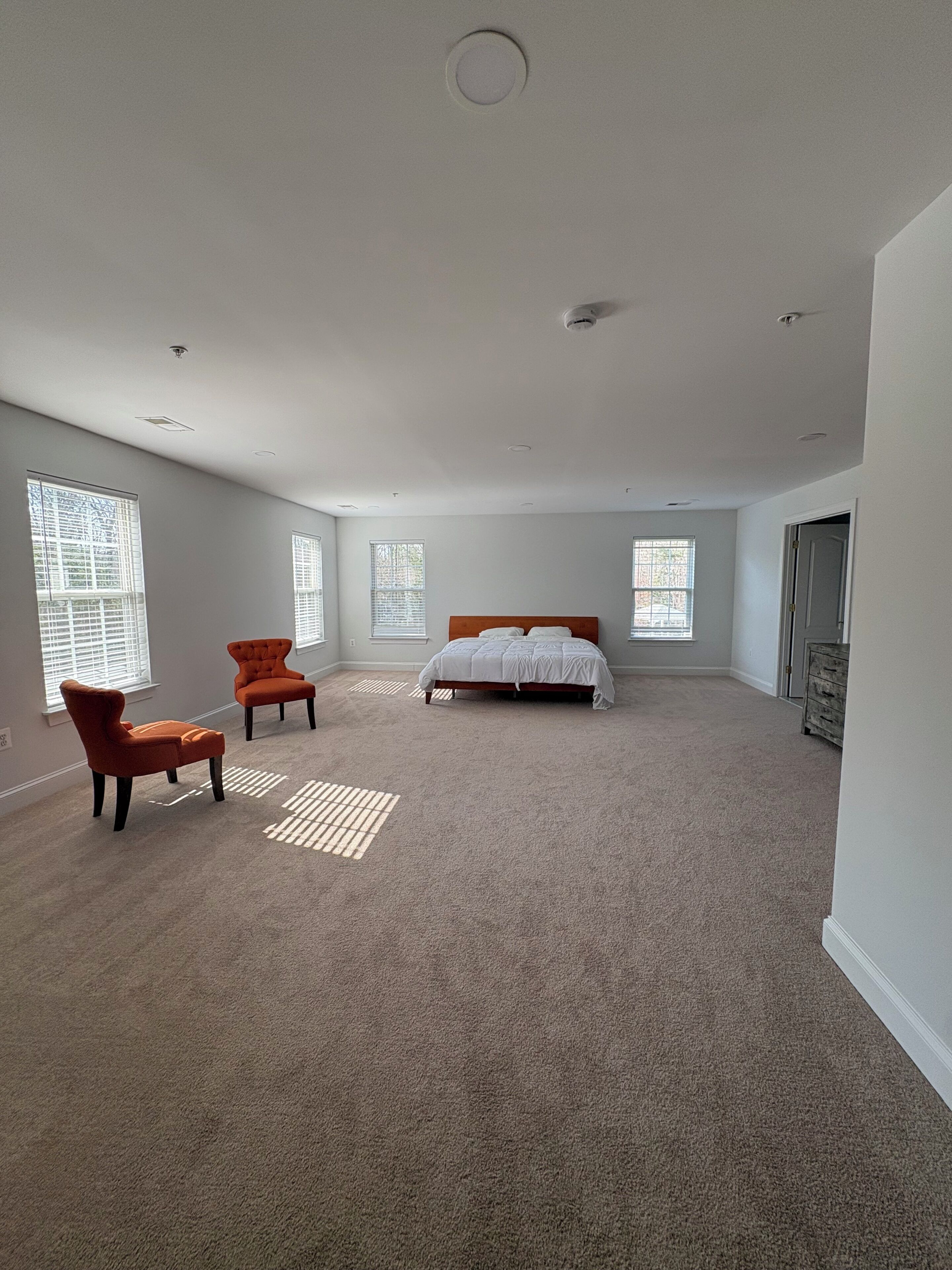 A spacious bedroom with a large bed, two chairs, and multiple windows.