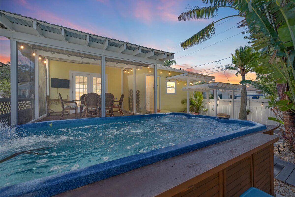A hot tub with a wooden deck, a covered patio area, and a view of the sunset.