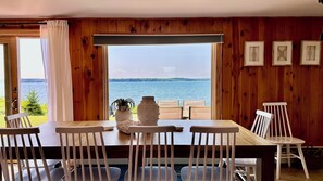 Comedor con vista al agua, paredes de madera y cuadros enmarcados.