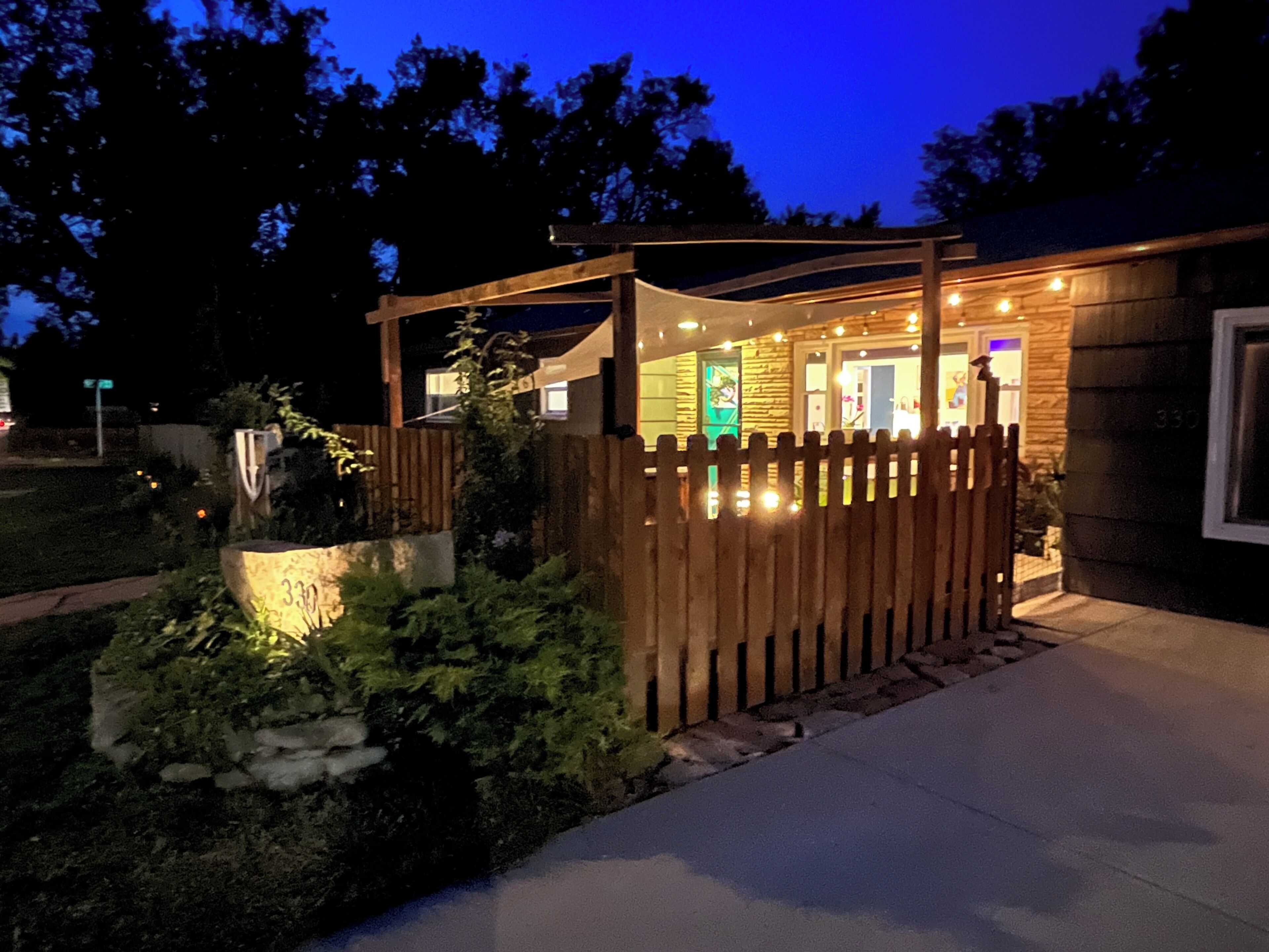 Una casa con cerca de madera, camino de entrada pavimentado y entrada bien iluminada.